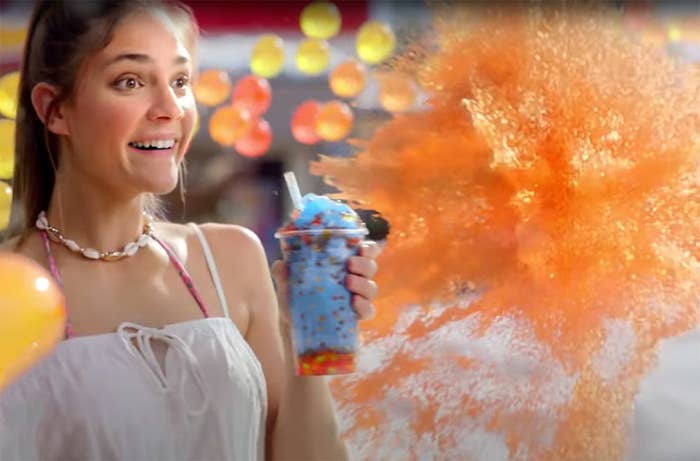 Woman holding a rainbow bursties drink smiling as a colourful explosion, signifying flavour, explodes next to her