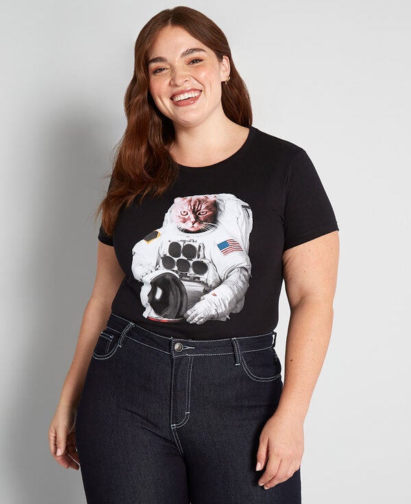 A model wearing the black tee featuring a print of a cat dressed as an astronaut