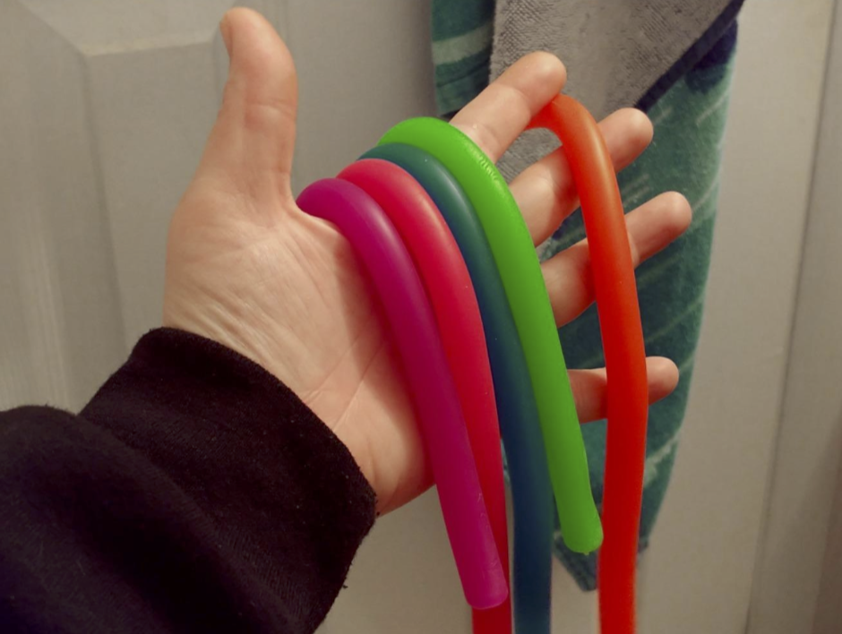 Reviewer&#x27;s hand holding five monkey noodles. They look like long, thick straws but have a gummy texture.