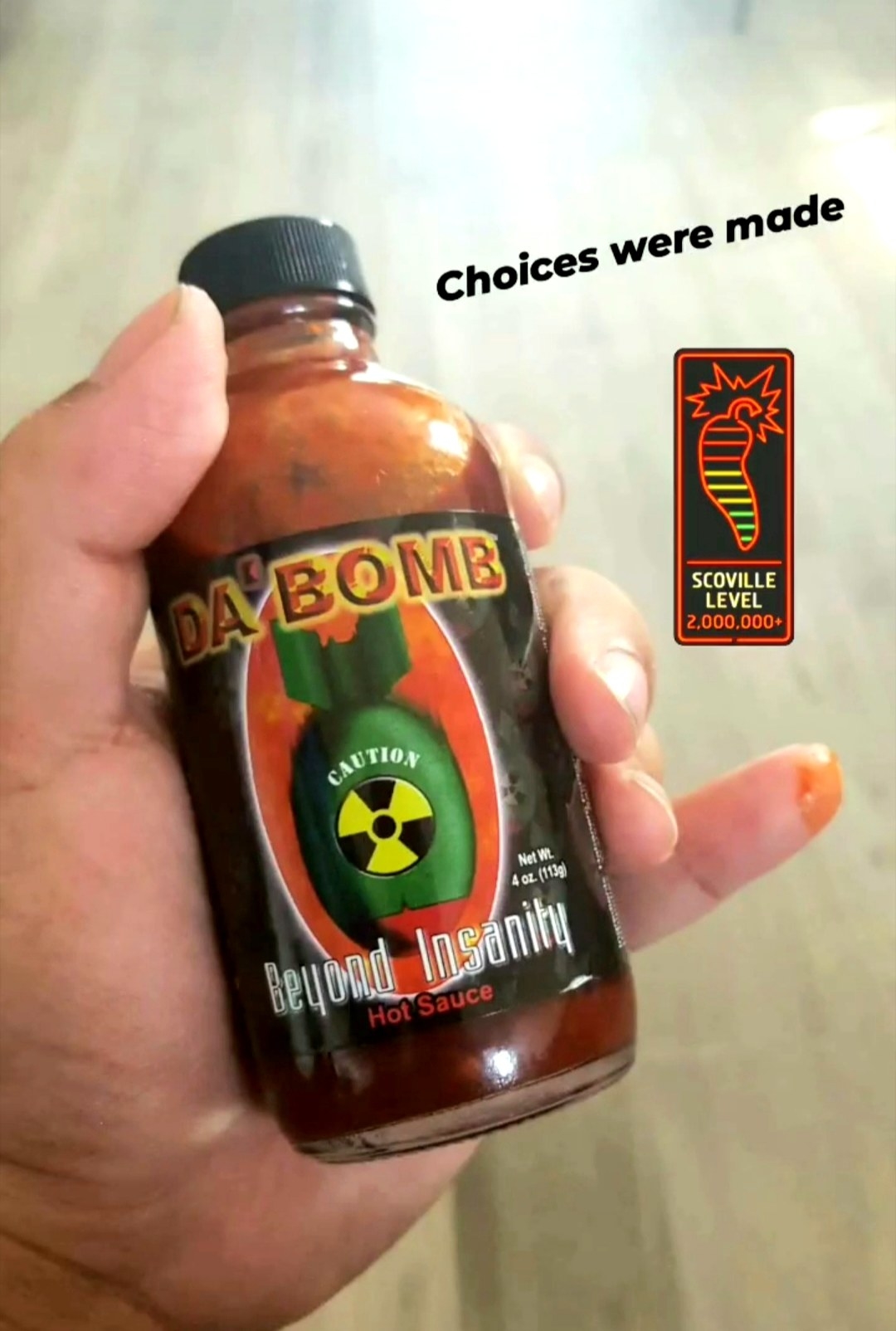 Sarah holding a bottle of Da Bomb Beyond Insanity hot sauce, the photo has the caption that says Choices were made