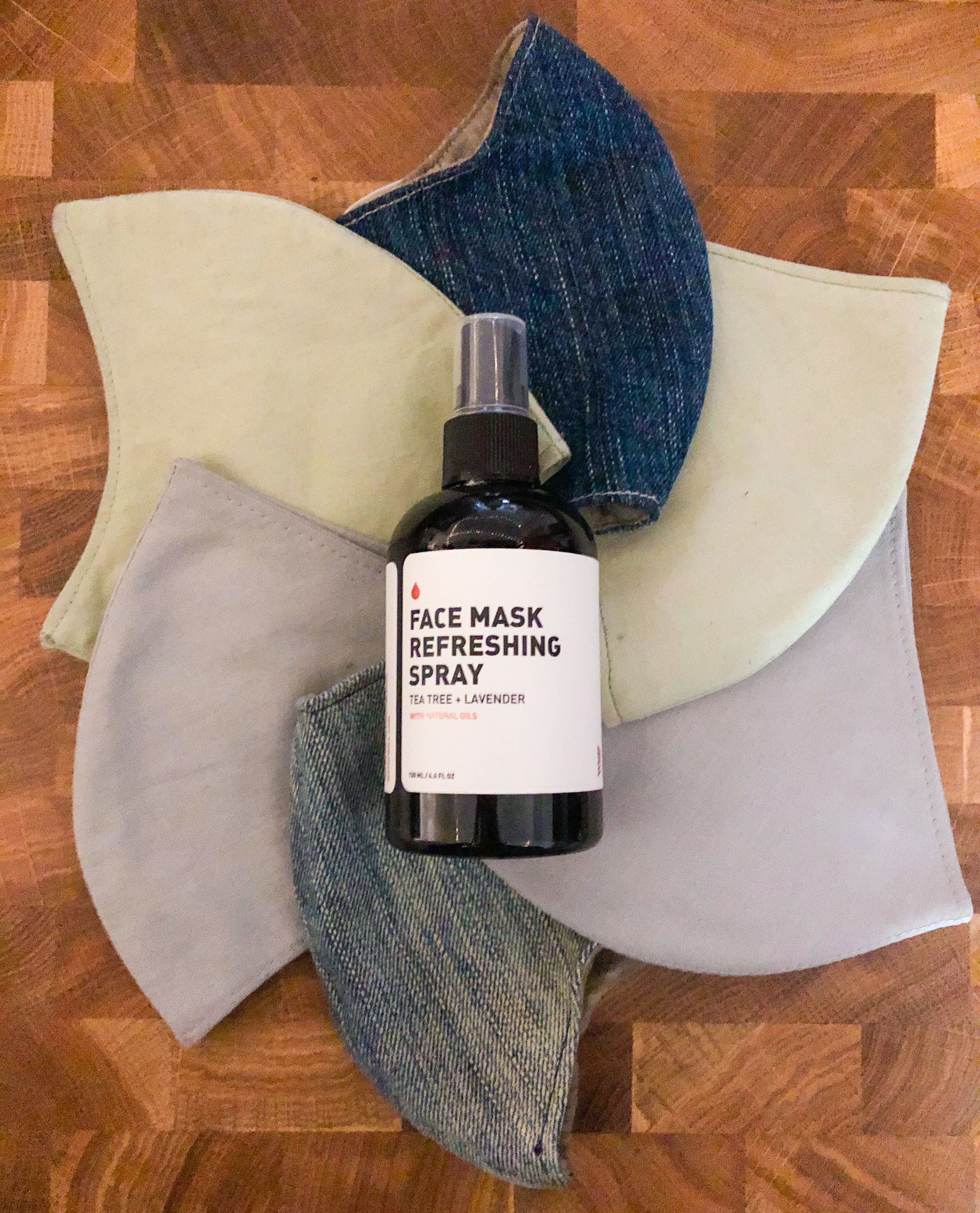 A bottle of face mask refreshing spray resting on top of several cloth face masks