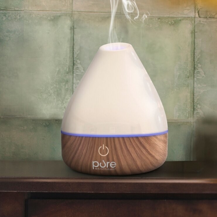 an essential oil diffuser with a white top and brown wooden base on a nightstand