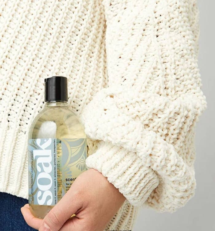 A close up of a person holding a bottle of the soap against a chunky knit sweater