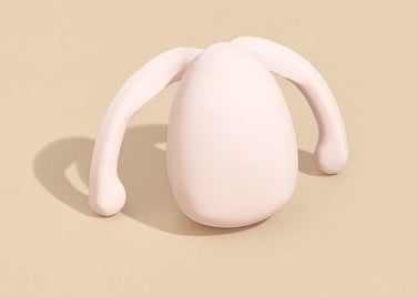 The pale pink, egg-shaped toy with curved wings coming out of the pointed tip