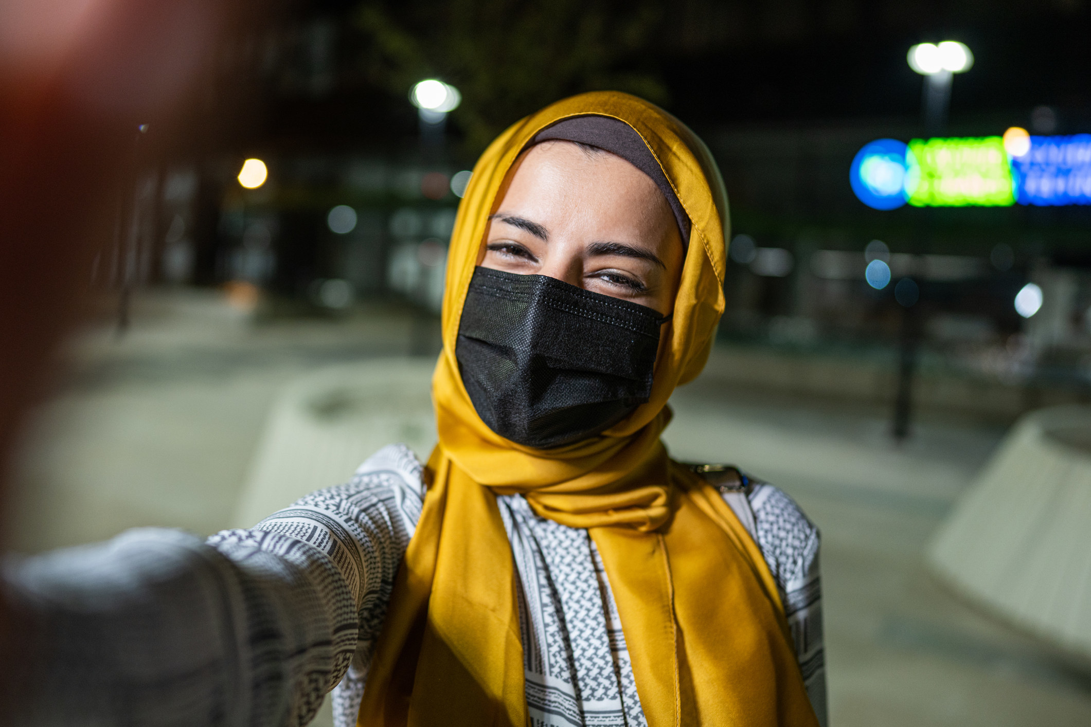 Une femme portant un masque et un foulard de tête, prenant un égoportrait.