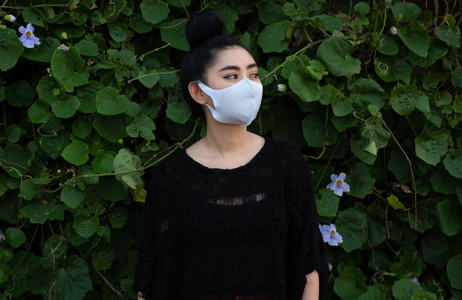 A person wearing a mask against a leafy backdrop.