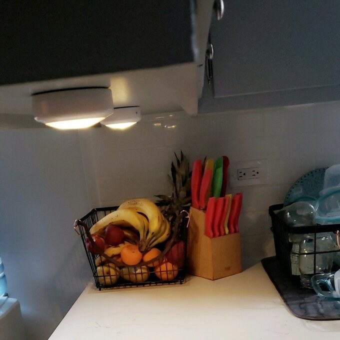 Reviewer&#x27;s picture of the puck lights attached to their kitchen cabinets 