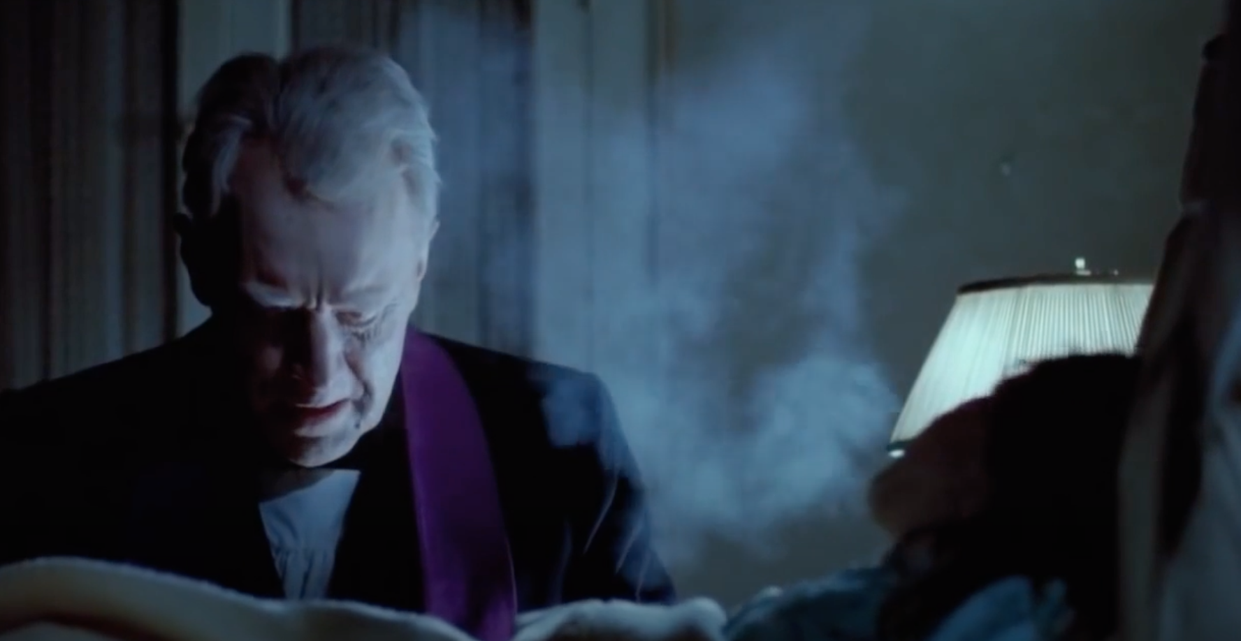 A priest sits next to young girl while performing an exorcism.