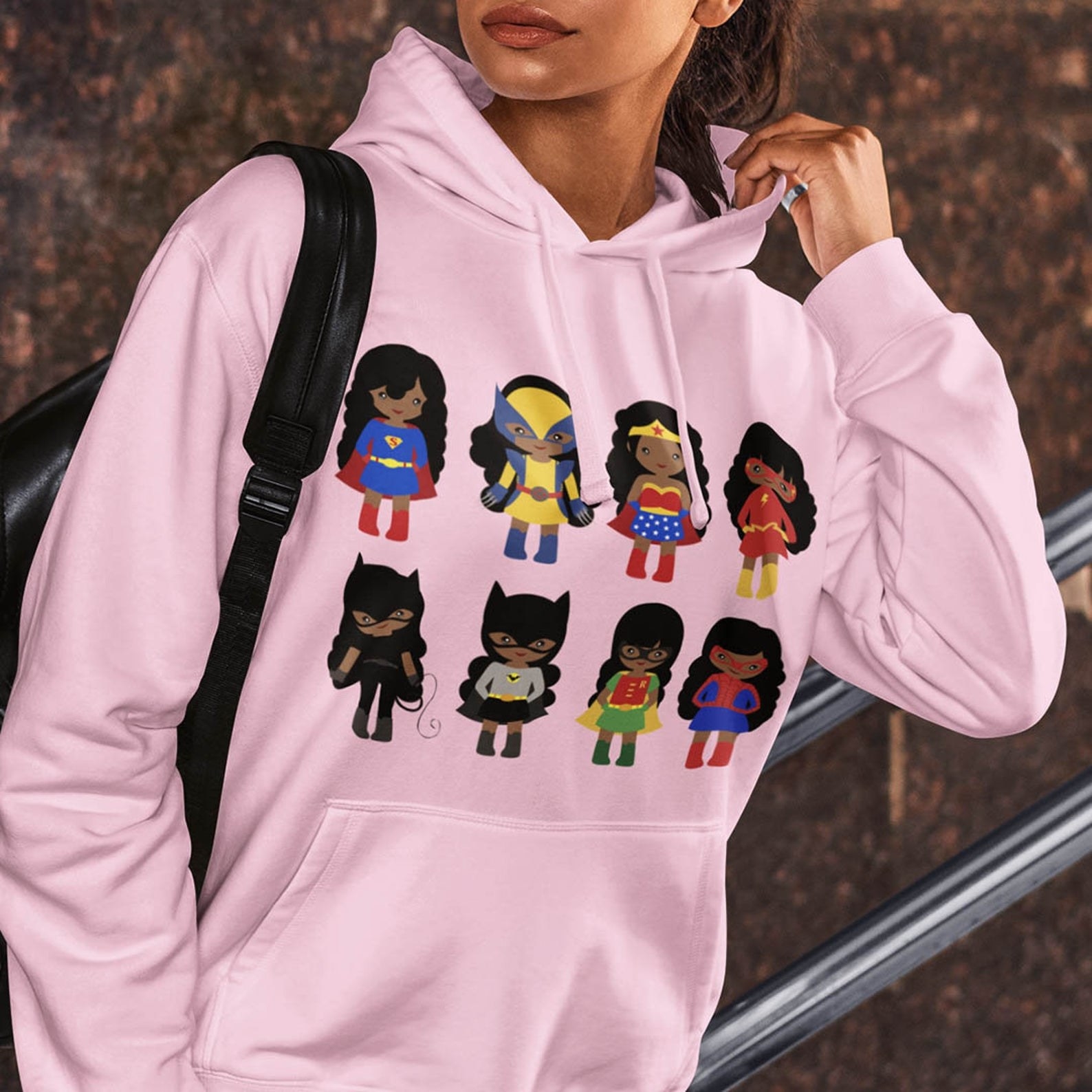 pink hoodie with brown-skinned cartoon superheros including Superman, Wolverine, Wonder Woman, Flash, Bat Girl, Catwoman, Robin, and Spider-Man