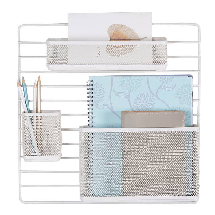 The organizer, which is a slatted white metal rectangle, with one large, one small, and one long but shallow mesh pocket hanging from it