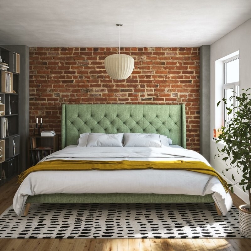 A sage green upholstered bed frame with tufted headboard