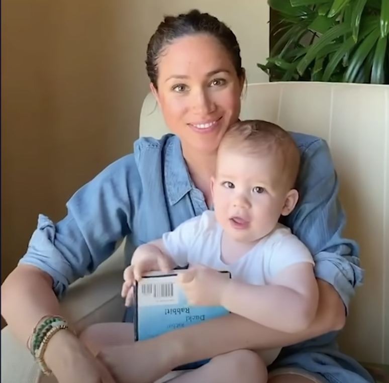 Meghan reading a book to Archie while he sits in her lap 