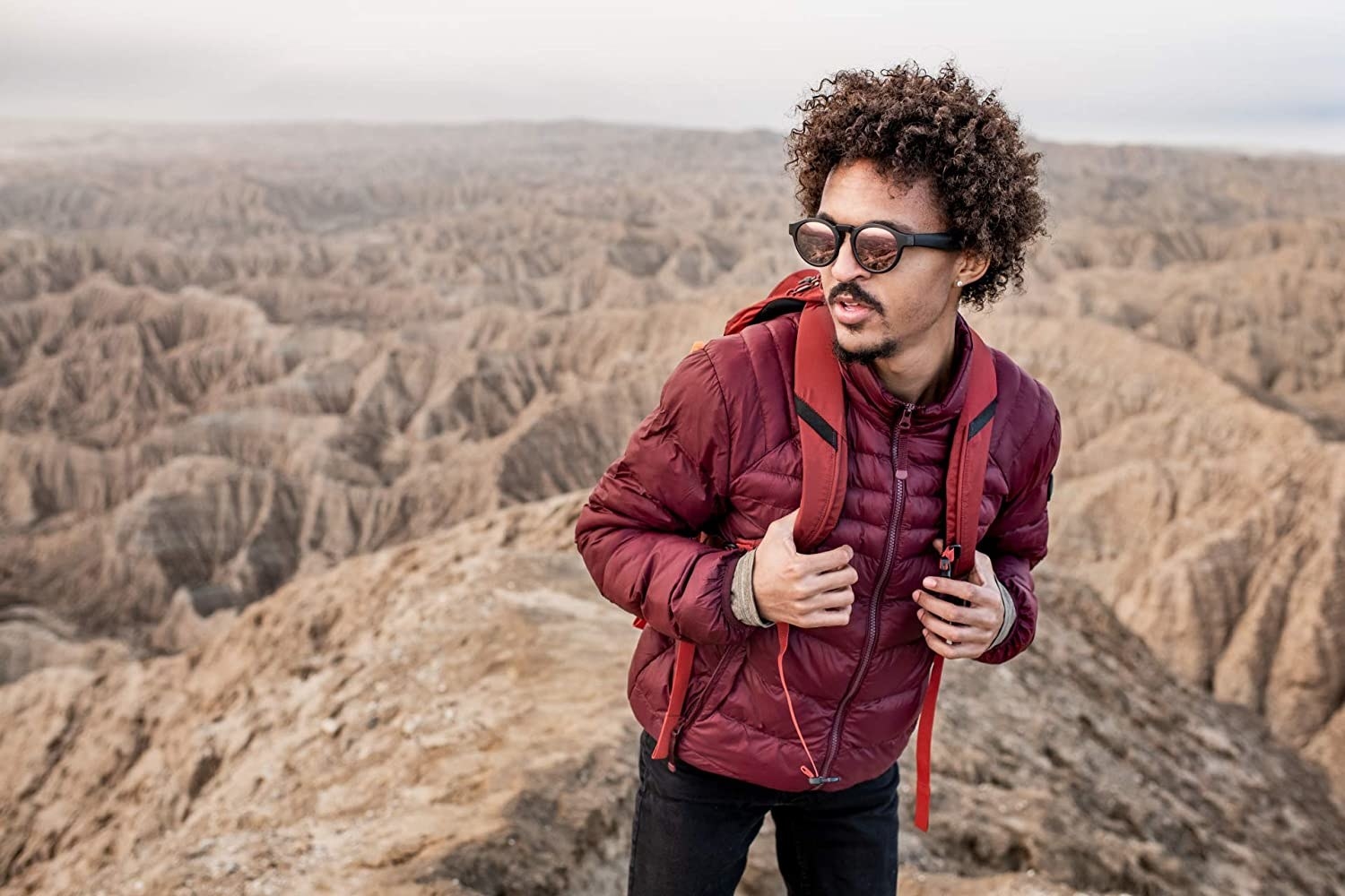 A person at the top of cliff wearing a jacket, backpack and sunglasses
