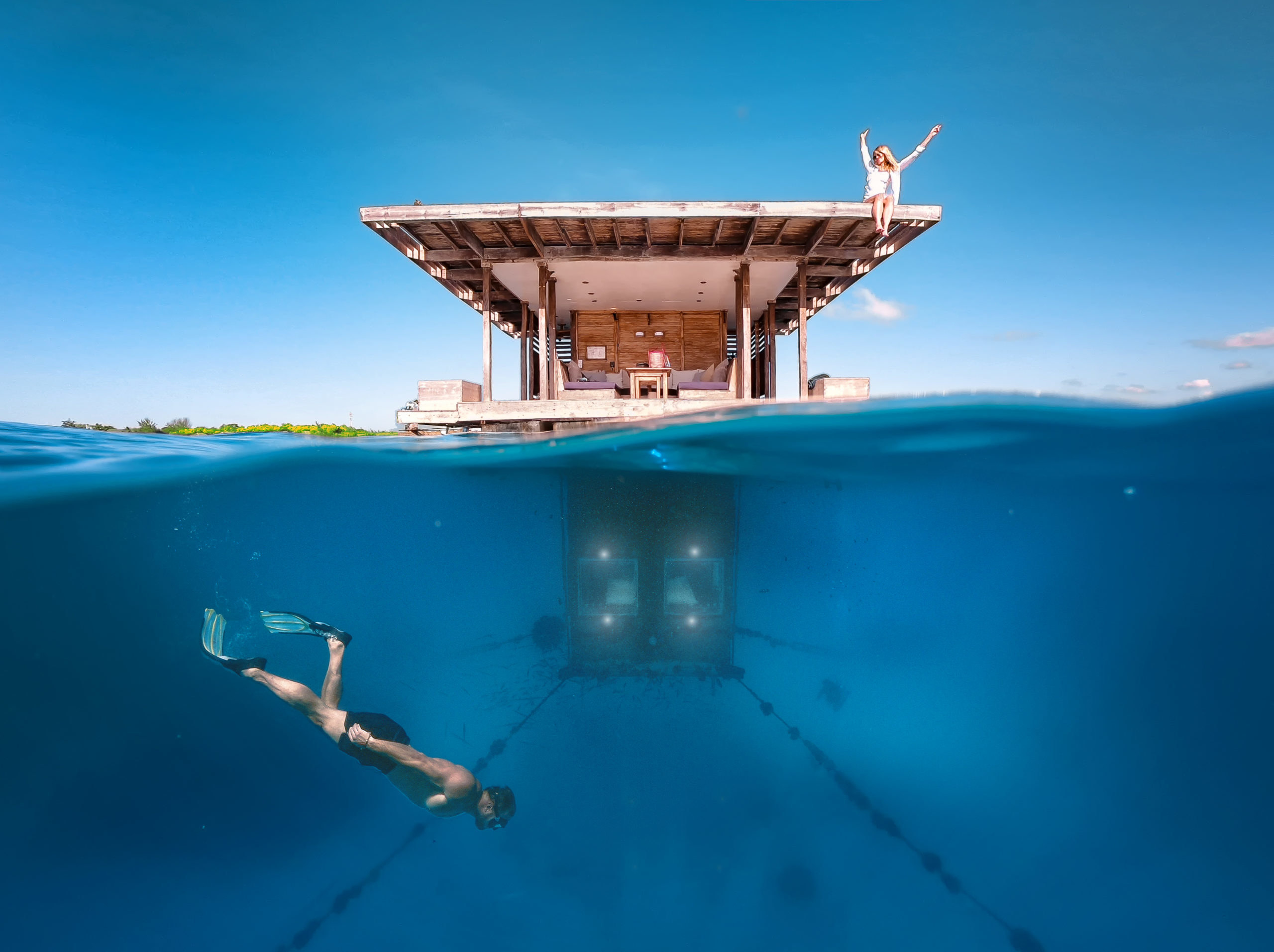 A floating house, showing a woman sitting on the roof, and a man swimming in the water underneath