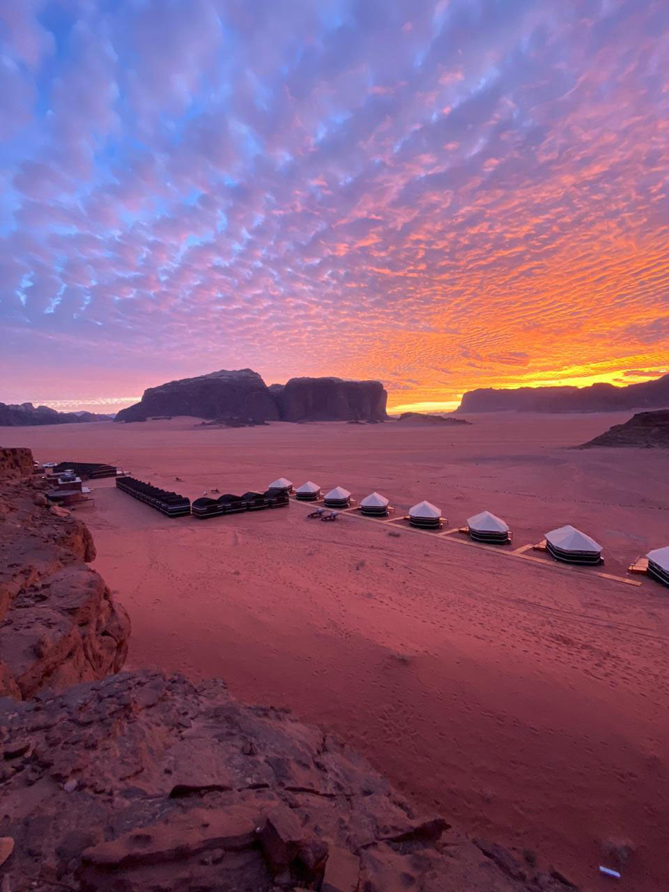 A purple and orange sunset over the desert where permanent tents are set up among sand dunes