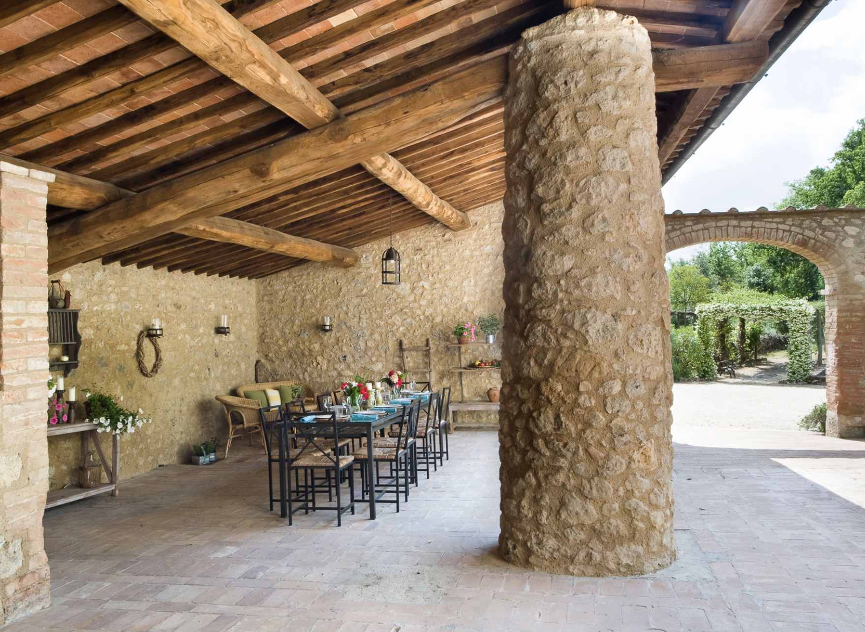 An outdoor patio of a stone and timber house surrounded by green trees