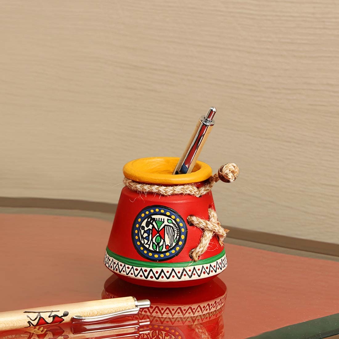 A red Warli pot with some pens in it