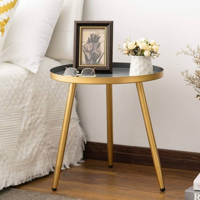 The circular table in a gold metallic tone holding a small flower pot, glasses, and a photo frame