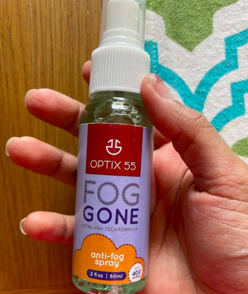 A reviewer holding the bottle of anti-fog spray
