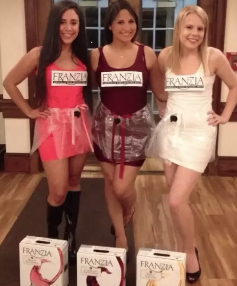 Three people dressed in different-colored dresses with saran wrap, spouts, and Franzia labels