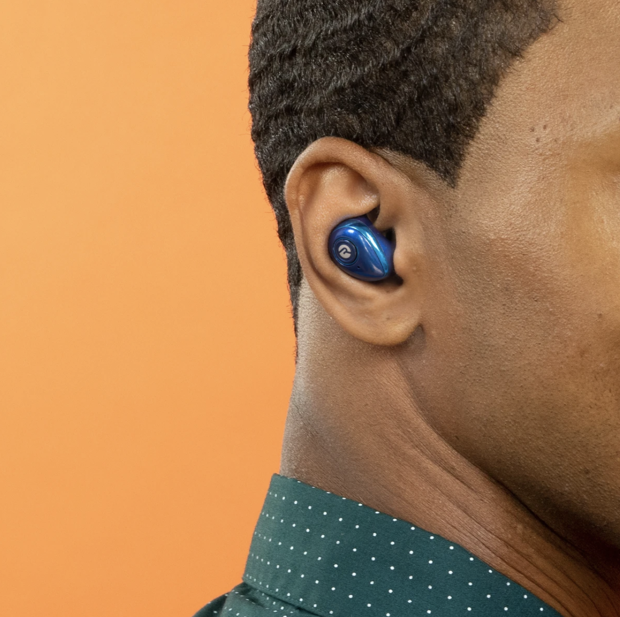 The small wireless earbud in blue in a model&#x27;s ear