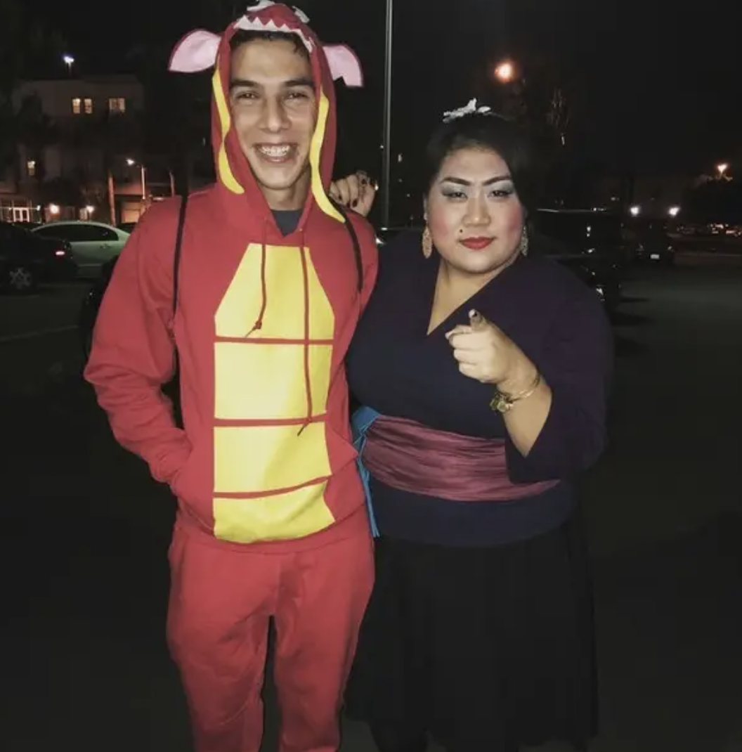 One person wearing red sweats with a hood as a dragon&#x27;s mouth, and another dressed as the Matchmaker from &quot;Mulan&quot;