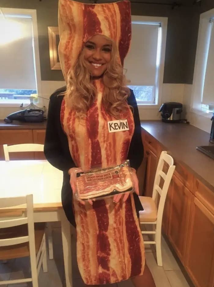 A woman dressed as a strip of bacon, holding bacon, wearing a name tag that says &quot;Kevin&quot;