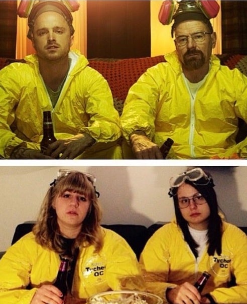 Two women dressed in hazmat suits with goggles on their heads and holding beer bottles.
