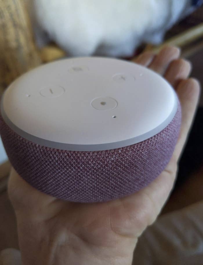 reviewer&#x27;s hand holding the Echo Dot which is circular and a pink color
