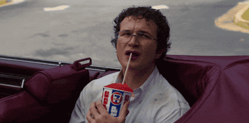 GIF of Alexei from Stranger things sitting in a convertible drinking a slurpee