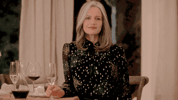A woman standing alone by a table with a wine glass