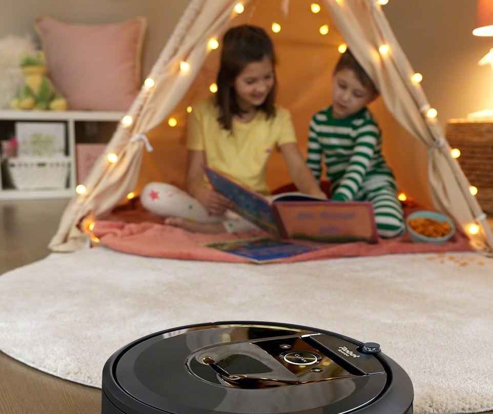 A Roomba sweeping a child's room with two children in a tent behind it
