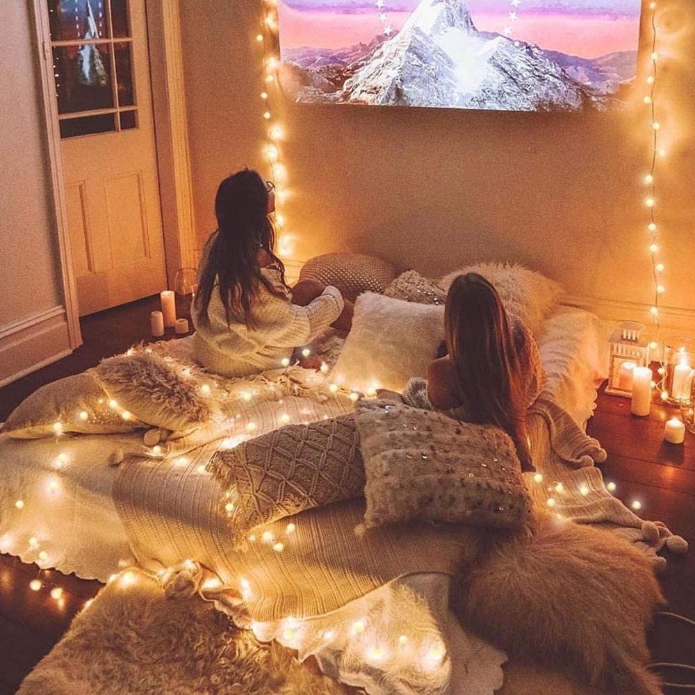 two people laying on a bed watching a movie with the lights draped around the bed for ambience 