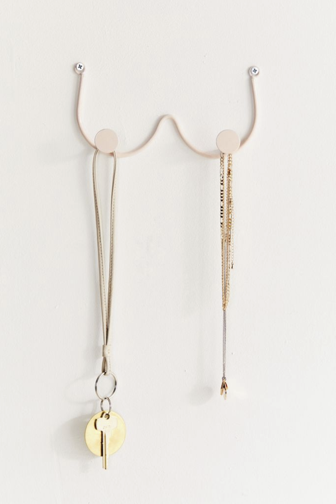 the rack with golden circular nipples that serve as the hooks. a necklace is hanging from one nipple while a key lanyard hangs from the other.