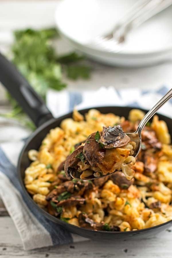 A skillet filled with spaetzle in a creamy mushrooms sauce and sliced mushrooms. 