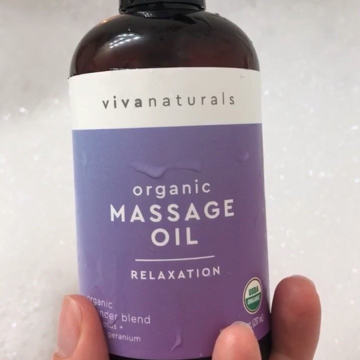 A person holding a bottle of the massage oil against a bubble bath backdrop