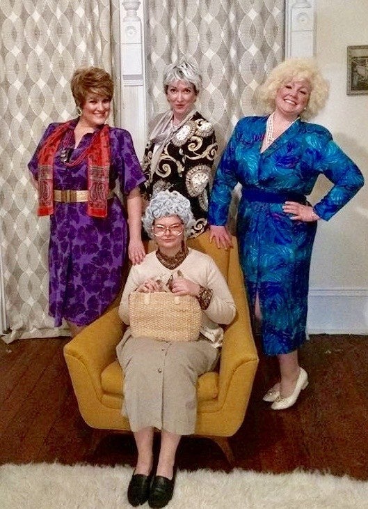 Four women dressed in printed vintage '80s outfits with shoulder pads, appearing to look like old women. They all have short wigs on.