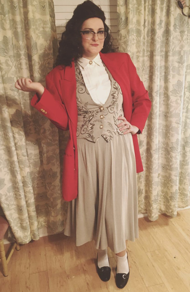 A woman in a wig wearing a blazer with shoulder pads and a vintage '80s-looking vested power suit.