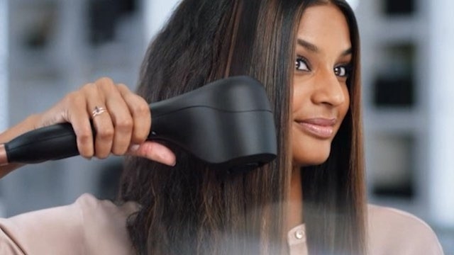 A smiling person uses the tool to smooth out their hair