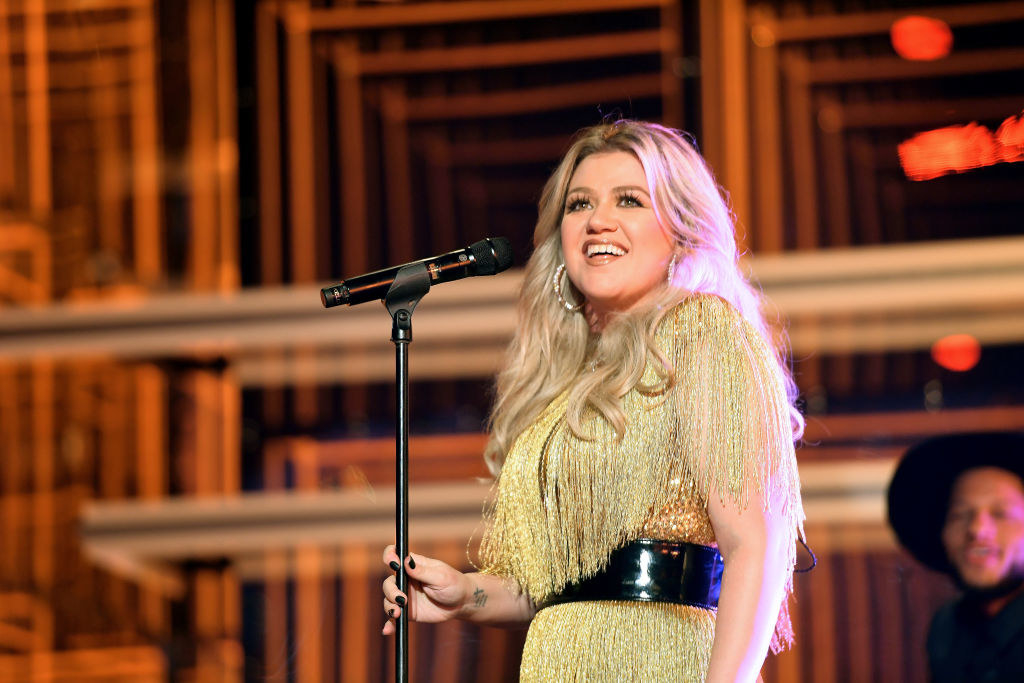 Kelly smiling onstage next to a microphone