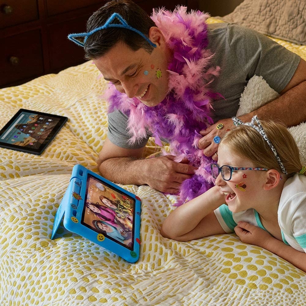 A child and parent lying on a bed watching a show from a small tablet