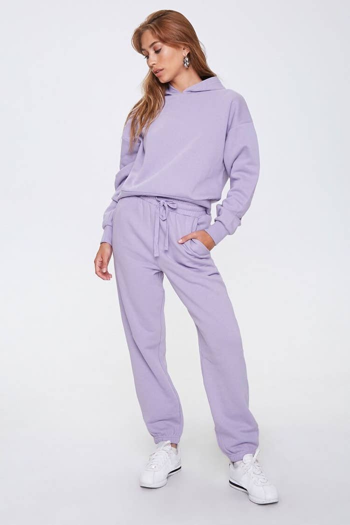 Model wears matching lilac fleece hoodie and joggers set with white sneakers