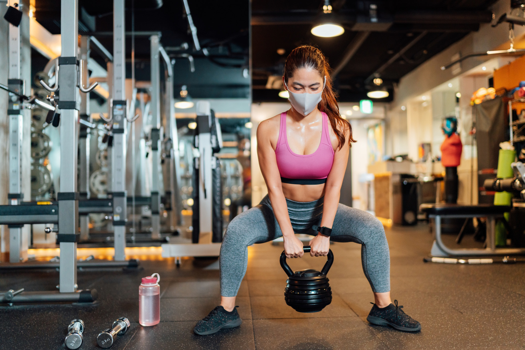 Une personne qui soulève un poids à la salle de sport, en portant un masque.