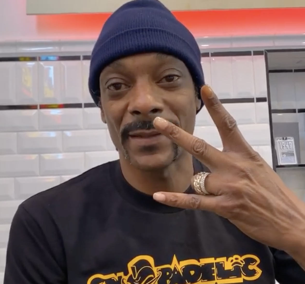 Snoop talking and holding up his hand in a W shape