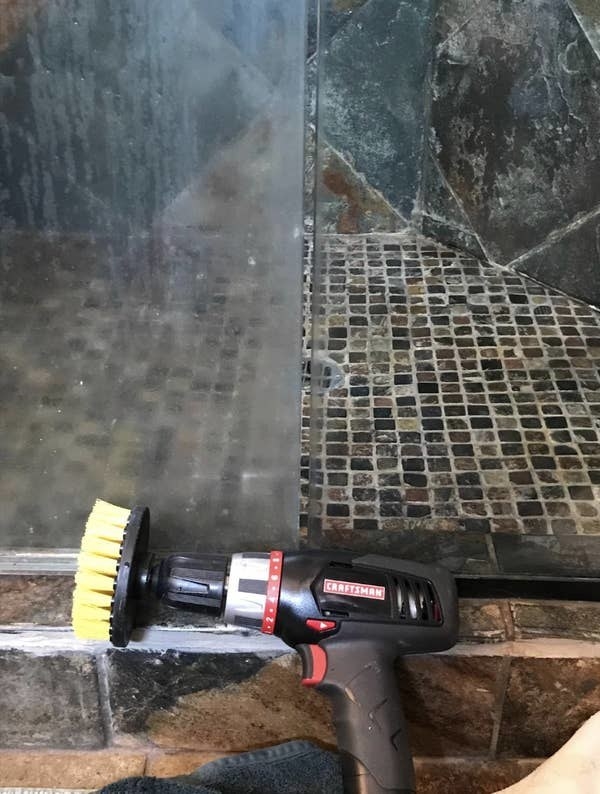 one of the brushes attached to a drill next to a shower pane with half still fogged up and the other super clear