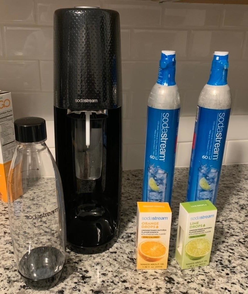 Reviewer pic of the SodaStream machine, two Co2 canisters, two clear bottles and lime and orange flavor drops