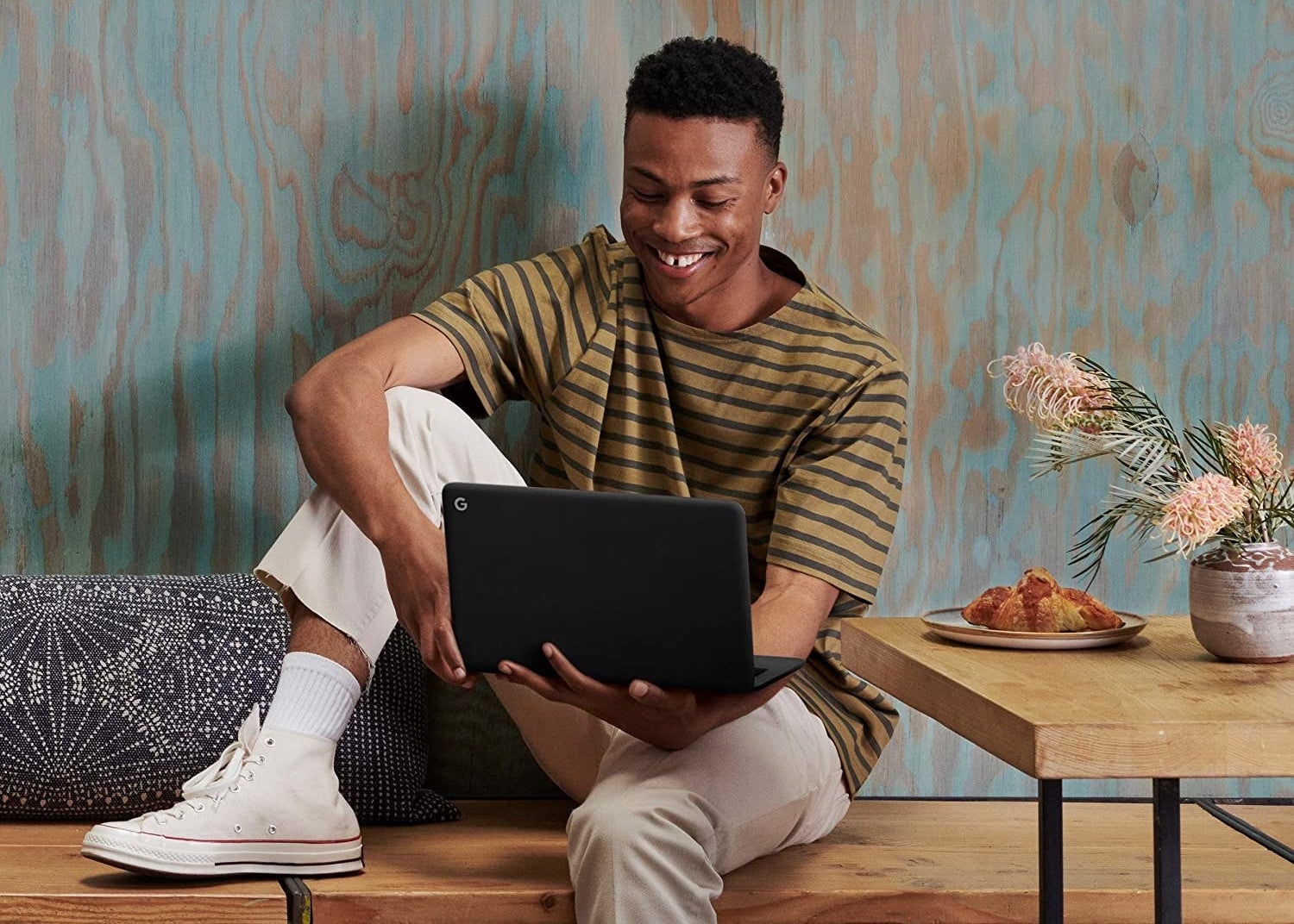 A person sitting on a wooden bench and balancing a small laptop on their hand