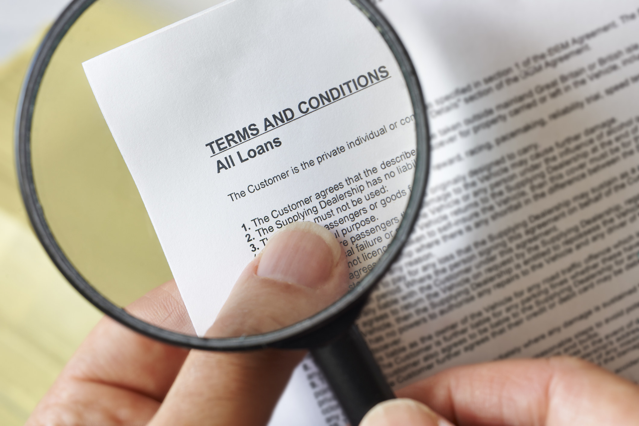 A magnifying glass reflects a contract reading &quot;terms and conditions, all loans&#x27;