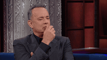 Tom Hanks rubs his hand against his face in a thinking motion