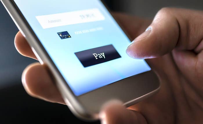 A closeup of a phone app with a thumb nearing the &quot;pay&quot; button